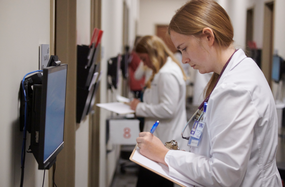 A student in a white coat taking notes.